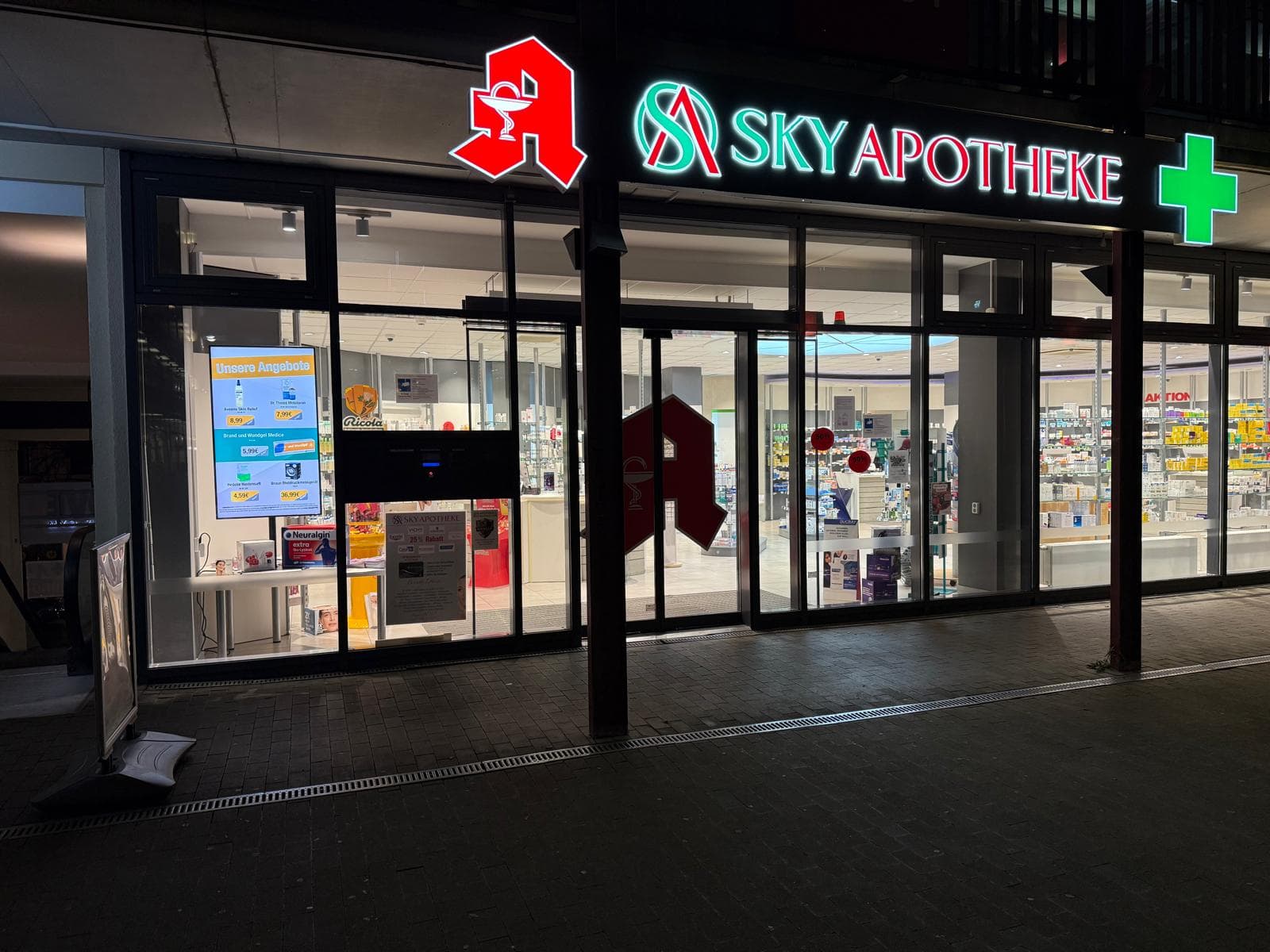 Sky Apotheke Kreuzberg mit beleuchtetem Schaufensterdisplay am Abend
